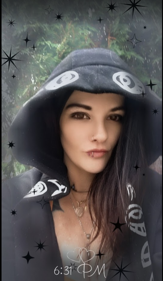 Mia Rae, founder of Moon & Mother, in the woods wearing a hooded cloak surrounded by stars