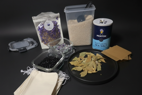 DIY spell bag ingredients flat lay — blue lotus flowers, crystal chips, Basmati rice, sea salt, bay leaves, and parchment scrolls