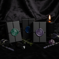 Three dark apothecary boxes with crescent moon wax seals on black velvet with crystals and candle