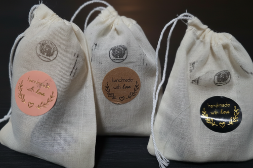 Three DIY Intention Spell Bags with peach, tan, and black handmade with love stickers on muslin drawstring pouches